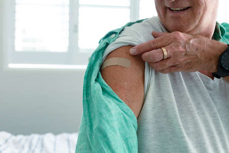 Midsection of smiling caucasian senior man with plaster on arm after vaccination. senior health and...