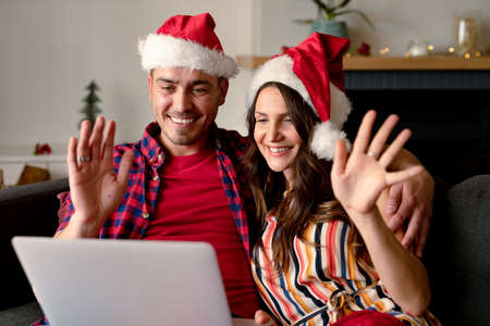 Happy caucasian couple wearing santa hats and having video call on laptop at christmas time. christmas, festivity and communication technology.の写真素材
