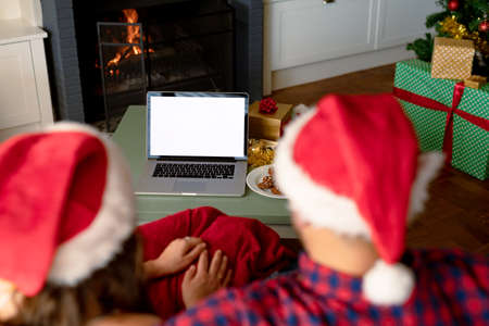 Back view of caucasian couple wearing santa hats, using laptop with copy space at christmas time....