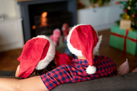 Back view of caucasian couple wearing santa hats and christmas socks at christmas time. family christmas time and festivity together at home.の写真素材