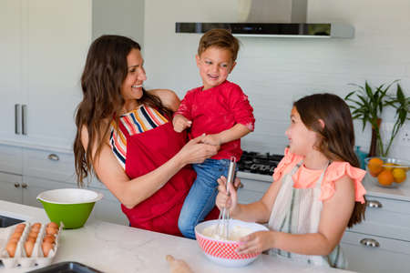 Happy caucasian mother, daughter and son baking together, making cookies in kitchen. family time,...