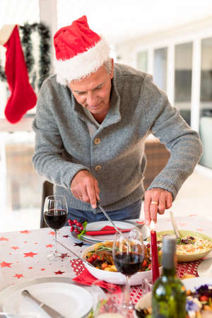 Happy caucasian senior man cutting food at christmas table. family christmas time and festivity together at home.の写真素材