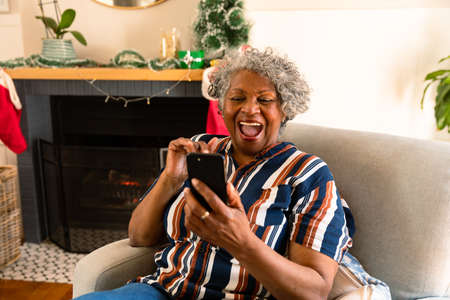 Happy african american senior woman sitting in armchair and having video call. healthy retirement...