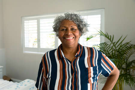 Happy african american senior woman standing in bedroom and looking at camera. healthy retirement...