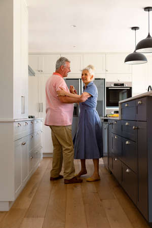 Happy caucasian senior couple dancing together in kitchen and having fun. healthy retirement lifestyle at home.の写真素材