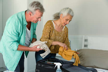 Caucasian senior couple packing suitcase together and talking in bedroom. travel preparation during covid 19 pandemic.の写真素材