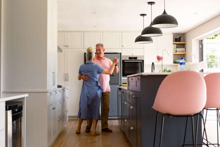 Happy caucasian senior couple dancing together in kitchen and having fun. healthy retirement lifestyle at home.の写真素材