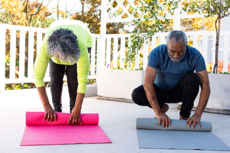 Smiling african american senior couple rolling yoga mats in garden. active and healthy retirement lifestyle at home.の写真素材