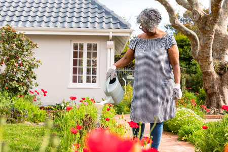 African american senior woman watering plants in backyard. active retirement lifestyle at home and...