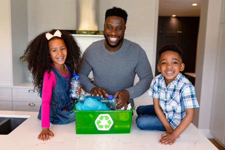African american father and children segregating rubbish in kitchen. recycling, family time, having fun together.の写真素材