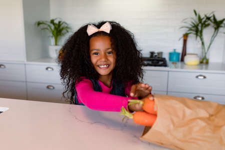 Happy african american girl unpacking groceries in kitchen. childhood, leisure and spending time at home.の写真素材