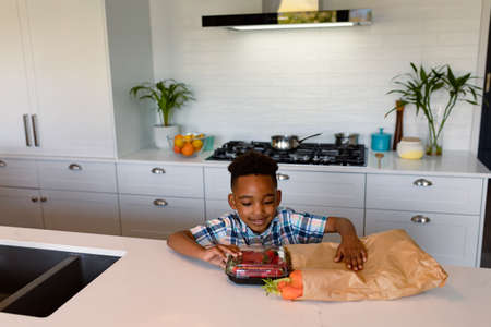 Happy african american boy unpacking groceries in kitchen. childhood, leisure and spending time at home.の写真素材