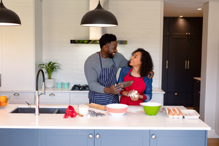 Happy african american couple wearing aprons, baking together and using tablet. family time, having fun together at home.の写真素材