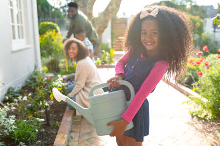 Happy african american girl and her family gardening and watering plants together. family time,...