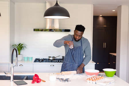 Focused african american man wearing apron, baking in kitchen. cooking and baking, spending time at home.の写真素材