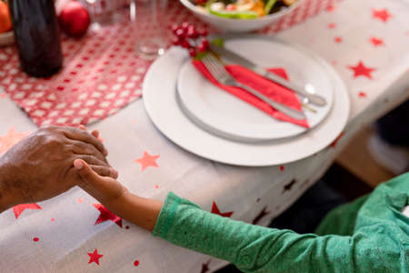 African american father and son holding hands over christmas table. christmas, festivity and tradition at home.の写真素材