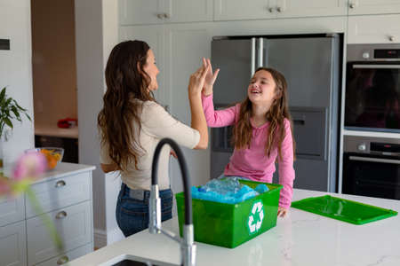 Happy caucasian mother and daughter segregating rubbish and giving high five. recycling, waste selection, spending time together at home.の写真素材
