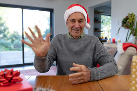 Caucasian senior man wearing santa hat having video call at christmas time. christmas, festivity and communication technology at home.の写真素材
