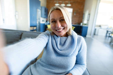Happy senior caucasian woman in living room sitting on sofa, making video call. retirement lifestyle, at home with technology.の写真素材
