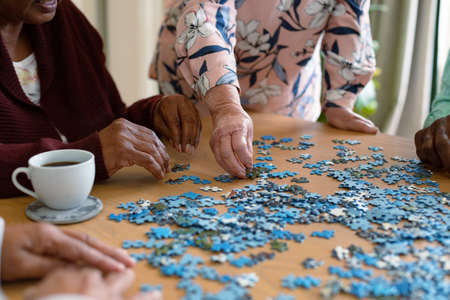 Hands of two diverse senior women and african american male friend doing puzzles. socialising with friends at home.の写真素材