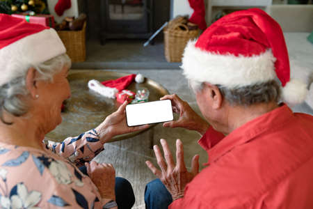 Caucasian senior couple wearing santa hats using smartphone with copy space at christmas time. christmas, festivity and communication technology.の写真素材