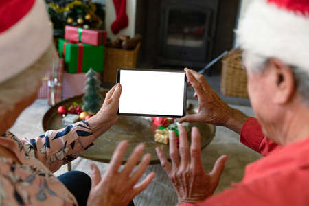 Caucasian senior couple wearing santa hats using tablet with copy space at christmas time. christmas, festivity and communication technology.の写真素材