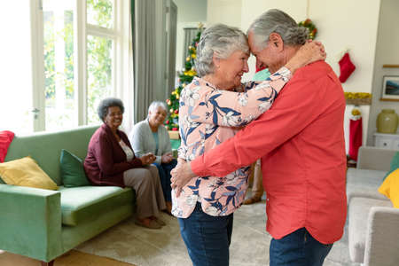 Happy caucasian senior couple dancing in front of their diverse friends at christmas time. christmas festivities, celebrating at home with friends.の写真素材