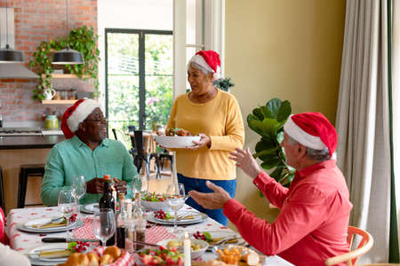 Diverse group of happy senior friends in holiday hats celebrating christmas together at home. christmas festivities, celebrating at home with friends.の写真素材
