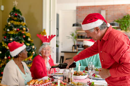 Diverse group of happy senior friends celebrating christmas with vine together at home. christmas festivities, celebrating at home with friends.の写真素材
