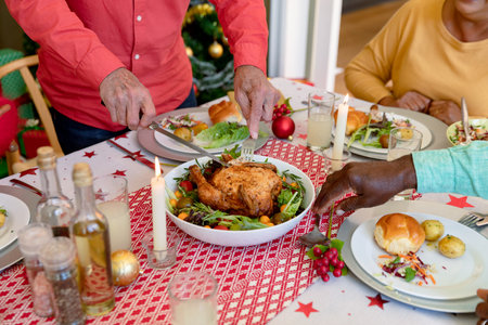 Hands of cauasian senior man cutting chicken at christmas table. christmas festivities and traditions, celebrating at home.の写真素材