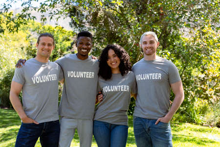 Group of smiling deverse female and male volunteers in matching tshirts looking at camera. eco conservation volunteers doing countryside clean-up.の写真素材