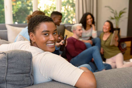 Happy african american woman having fun with diverse group of female and male friends at home. socialising with friends at home.の写真素材