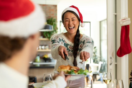 Happy asian woman in santa hat celebrating christmas with friends at home. christmas festivities, celebrating at home with friends.の写真素材