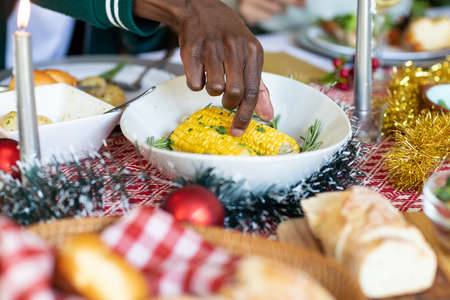 Hand of african american man taking corn from bowl at christmas table. christmas, festivity, tradition and celebrating at home.の写真素材