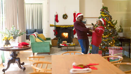 Happy african american senior couple in santa hats dancing at home at christmas time. retirement lifestyle and christmas festivities, celebrating at home.の写真素材