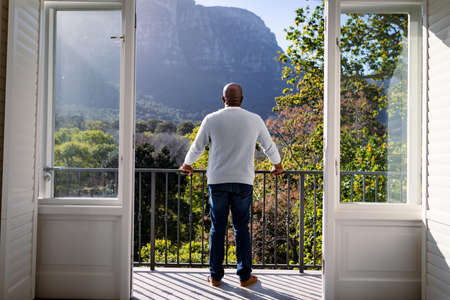 Back view of african american senior man standing on balcony and looking into distance. retirement lifestyle, spending time at home and garden.の写真素材