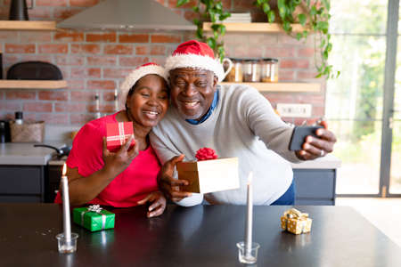Happy african american senior couple having video call on smartphone in kitchen at christmas time. retirement lifestyle, christmas festivities and communication technology.の写真素材