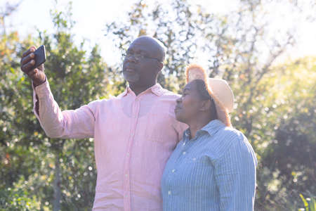 Happy african american senior couple taking selfie outdoors. retirement lifestyle, spending time at...