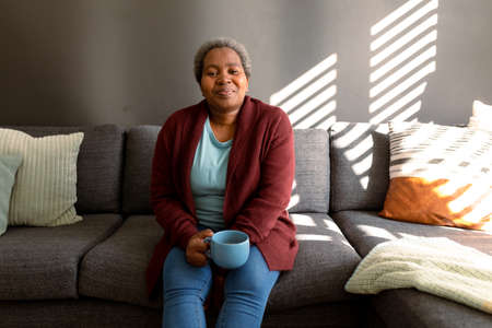 Relaxed african american senior woman sitting on sofa and drinking coffee. retirement lifestyle,...
