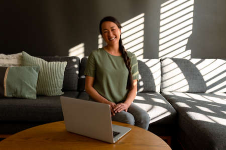 Happy asian woman sitting on sofa at home and using laptop. lifestyle, leisure and spending time at home.の写真素材