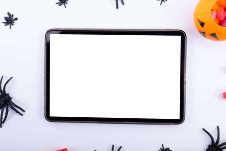 Composition of halloween spiders, pumpkin and sweets and tablet with copy space on white background....