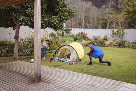 Caucasian father and son smiling while setting up a tent together in the garden. fatherhood and love...