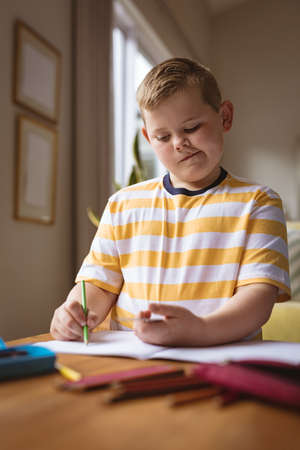 Caucasian boy drawing in his book sitting in the living room at home. childhood and hobby concept