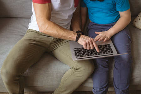 Mid section of caucasian father teaching his son to use laptop sitting on the couch at home. fatherhood, technology and home conceptの写真素材