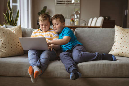 Two caucasian boys using laptop sitting on the couch at home. childhood, technology and home conceptの写真素材