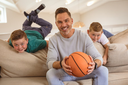 Portrait of caucasian father and two sons with basketball smiling at home. sports and entertainment conceptの写真素材