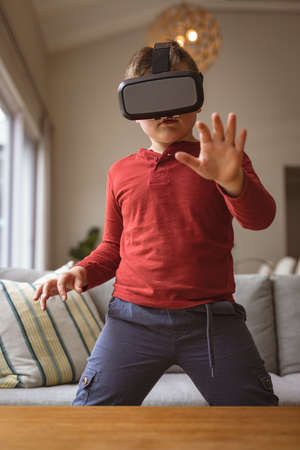 Caucasian boy wearing vr headset gesturing while sitting on the couch at home. gaming and...