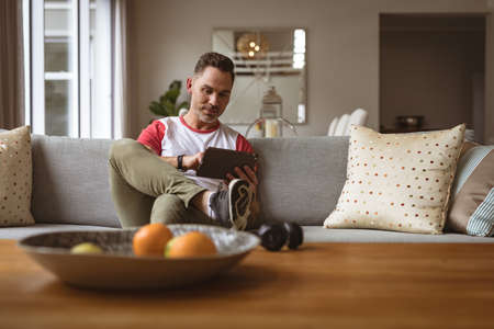 Caucasian man using digital tablet sitting on the couch at home. working from home during coronavirus covid-19 pandemic conceptの写真素材