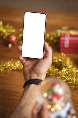 Hand holding smartphone with copy space against christmas gifts and decorations on wooden table. christmas festivity and celebration conceptの写真素材