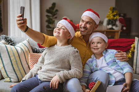 Caucasian father and two sons talking a selfie from smartphone at home during christmas. christmas...